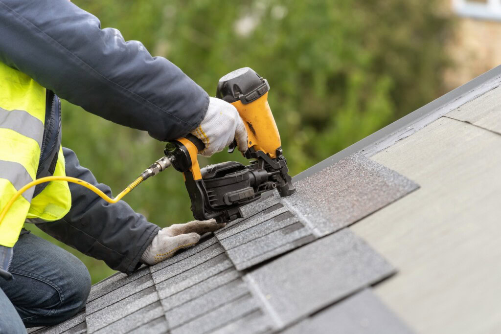 Roofer using nail gun to secure shingles to a roof