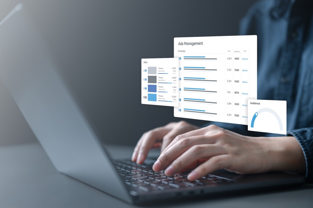Hands typing on laptop with ads management dashboard showing campaign budget, daily spend, audience targeting, and performance control for digital advertising